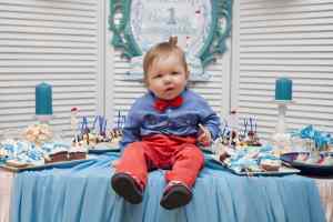 A baby boy sitting on the table surrounded with cupcakes for his 1st birthday