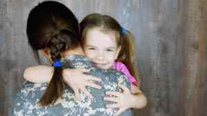 a little girl hugging her mom which is in a military uniform.