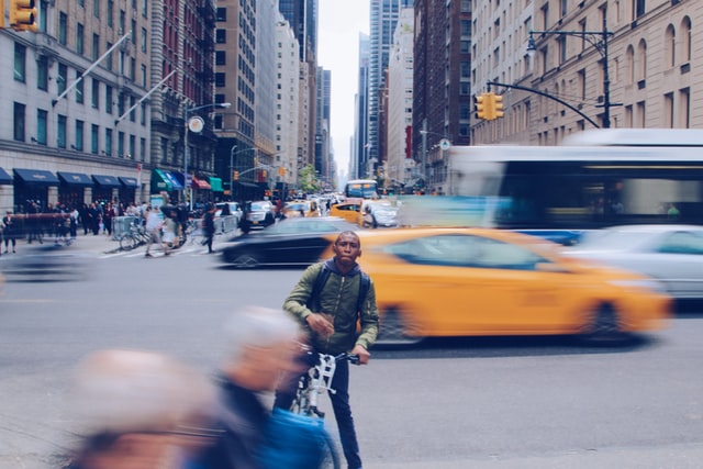 A man on a bicycle in NYC with a yellow taxi behind him