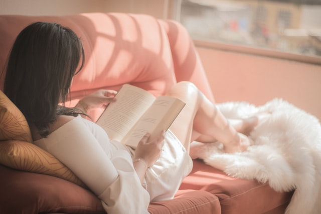 A woman laying on a sofa reading a book to overcome stress & anxiety in NYC