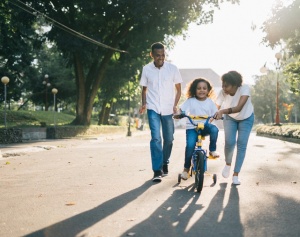 Parents teaching their daughter to ride a bike.