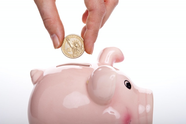 A person putting a coin in a pink piggy bank.