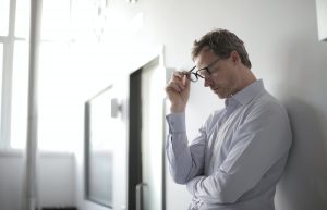 A stressed man taking off his glasses.