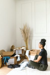 A woman sitting on the floor and looking at some items sorted into different cardboard boxes.